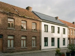 Verweerde bakstenen rijwoning met enkele beglazing links, geleidelijk overgaand in geïsoleerde gevel met zonnepanelen en dubbel glas rechts.