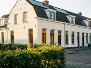 Geïsoleerde Nederlandse rijtjeswoning met dubbele beglazing en zonnepanelen op het dak, crèmewitte gevel in warm middaglicht.